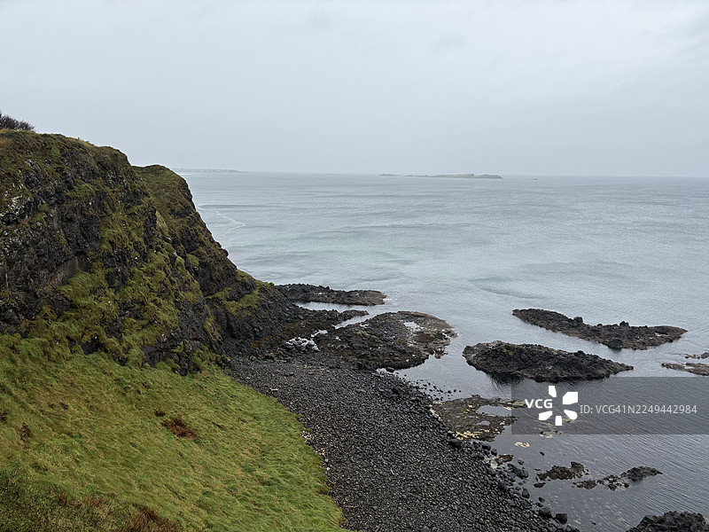 爱尔兰北部安特里姆海岸的邓路斯城堡，在阴天之下，有着崎岖的悬崖、岩石海滩和广阔平静的大海的戏剧性海景。图片素材