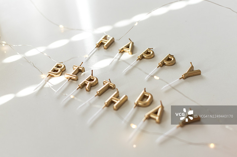 金色的生日快乐蜡烛和串灯在白色表面上，庆祝特别的时刻图片素材