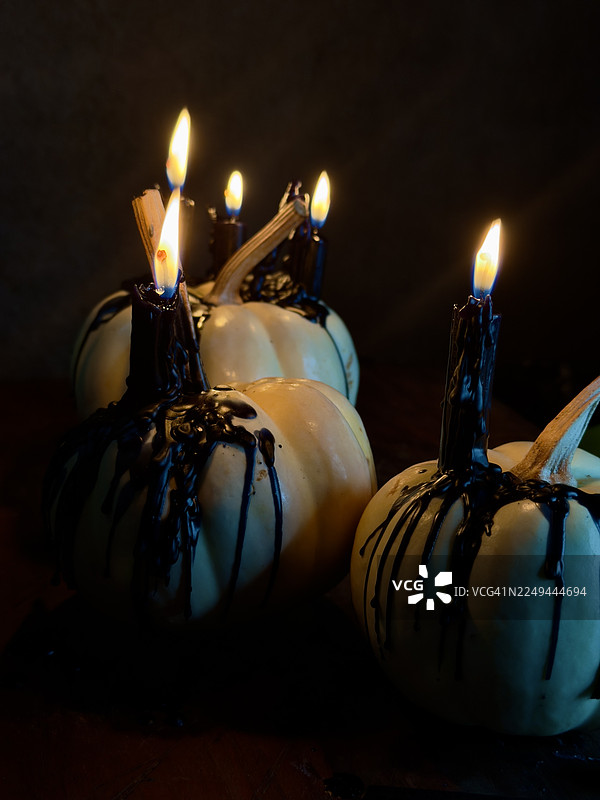 在黑暗、阴郁的氛围中，点亮的黑色蜡烛滴着蜡油在白色南瓜上，营造出万圣节或哥特式的感觉图片素材