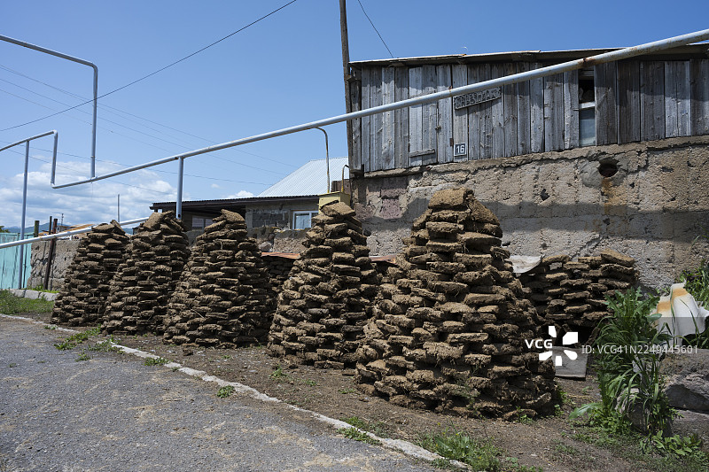 蓝天下，亚美尼亚盖加尔库尼克省塞万附近一栋木屋前堆叠的晒干的牛粪砖图片素材