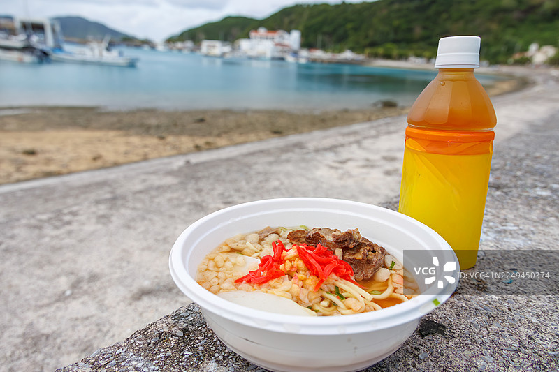 早餐享用一大碗冲绳荞麦面，上面铺满了炖至软嫩的红烧猪肋排（Sōki），淋上甜咸酱汁。搭配一杯三品茶（冲绳风味茉莉花茶）。地点在冲绳的座间味港，一个如热带天堂般的离岛。图片素材
