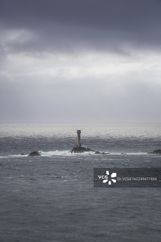 孤独的灯塔矗立在阴沉多云的海面上的一块岩石上，位于英国康沃尔郡的兰兹角。图片素材