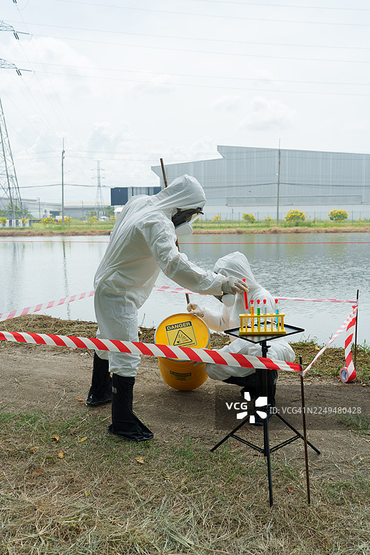 生态学家身着防护服，在养殖水生动物的农场池塘中检查水质，并采集水样进行分析。图片素材