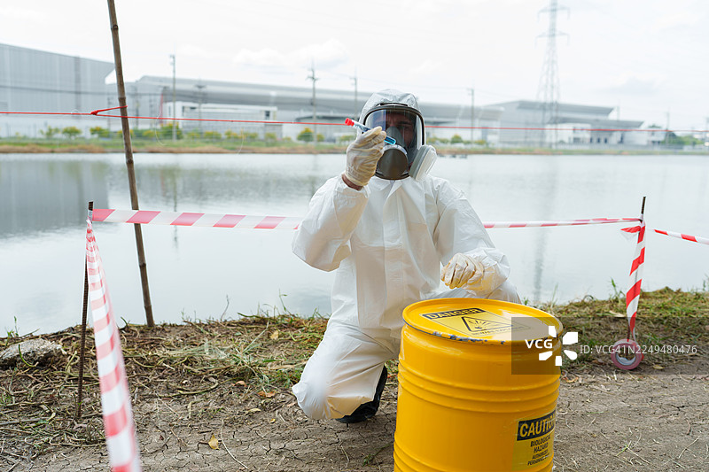 生态学家穿着防护装备，在养殖水生动物的农场池塘中检查水质，并收集水样进行分析。图片素材