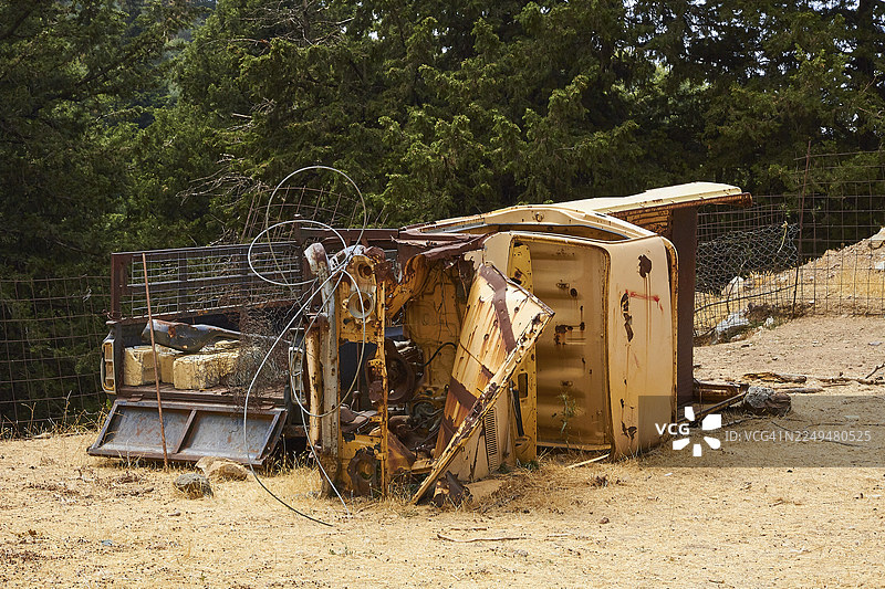 翻覆在树林中的生锈车辆，周围散落着扭曲的金属零件，希腊，希腊岛屿，克里特岛图片素材