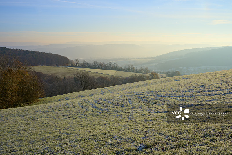 晨雾笼罩着绿色连绵的山丘，天空晴朗，位于德国黑森州奥登瓦尔德地区卢策尔巴赫的泽克瑙厄恩。图片素材
