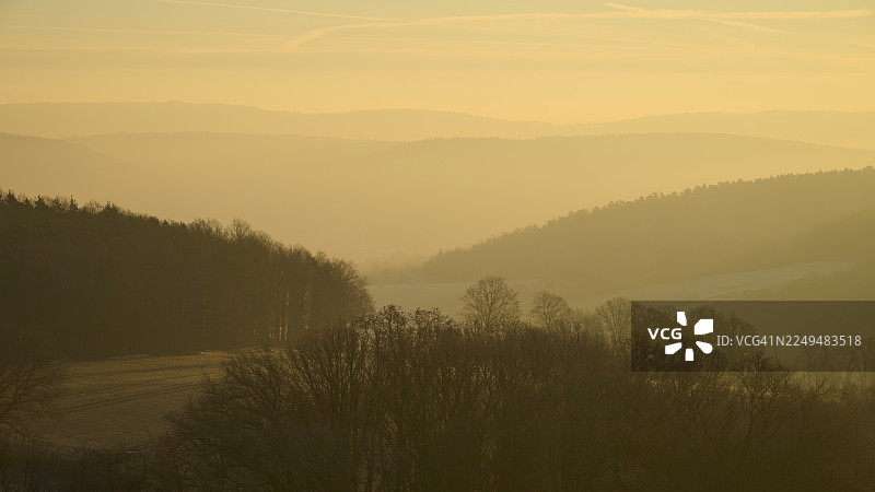 日出时分，晨雾笼罩下的模糊山丘与树木，金色的天空，德国黑森州奥登瓦尔德地区卢策尔巴赫的塞克马恩图片素材