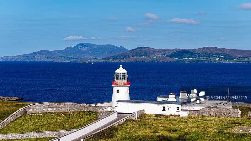 从空中俯瞰圣约翰角半岛,灯塔建筑群坐落于爱尔兰多尼戈尔郡崎岖的海岸线上,大西洋风光壮丽,远山隐约可见,体现了旅行、文化遗产与海上导航的概念。图片素材