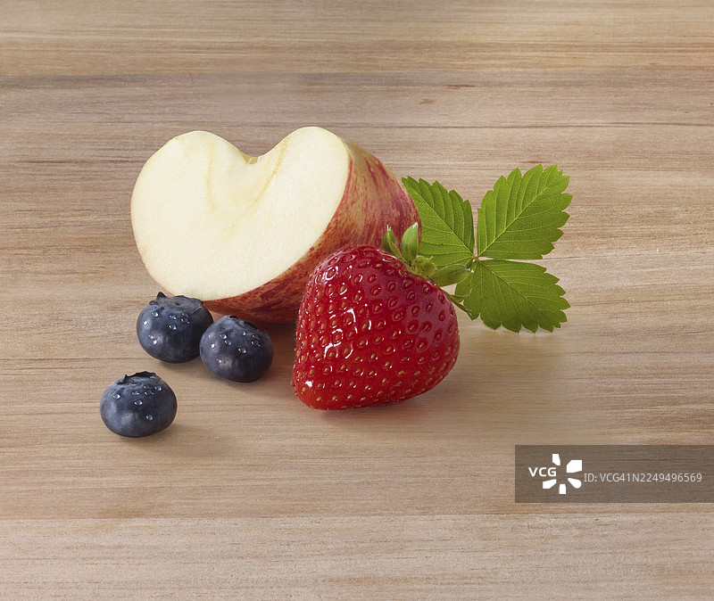 木桌上的苹果片（Malus domestica）、草莓（Fragaria）及草莓叶、蓝莓（Vaccinium myrtillus），棚拍图片素材