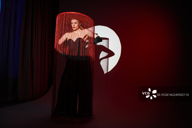 身着黑色礼服的模特，头戴红色礼帽，配有红色流苏面纱和手套的迷人时尚肖像。图片素材