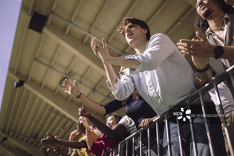 比赛日，仰视角度看年轻男子在体育场看台上欢呼图片素材