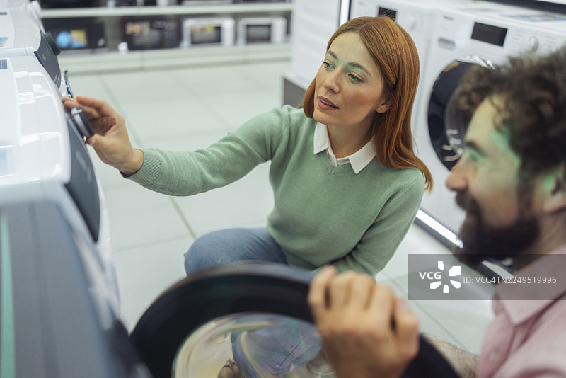 情侣在现代家电商店比较滚筒洗衣机图片素材