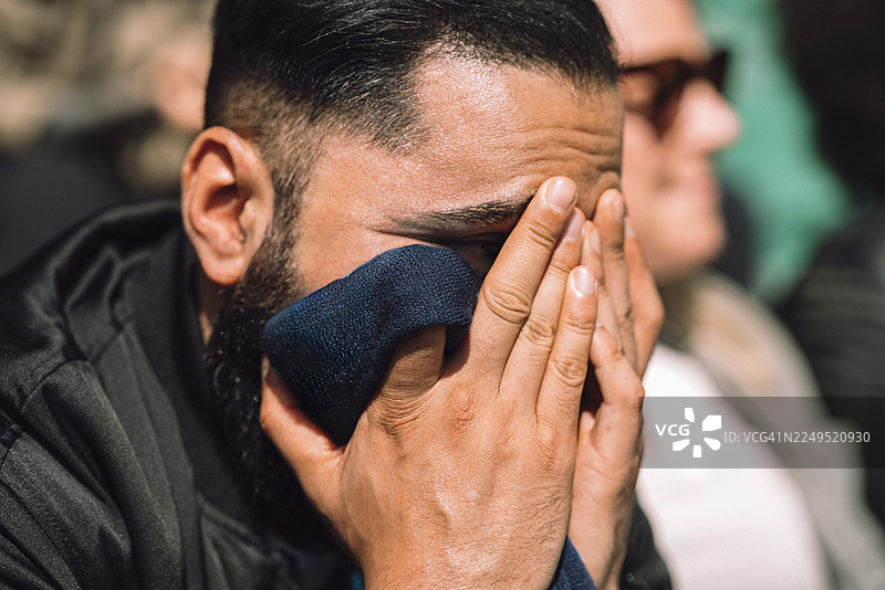 阳光明媚的日子里，体育场看台上一个男人双手抱头绝望的特写镜头图片素材