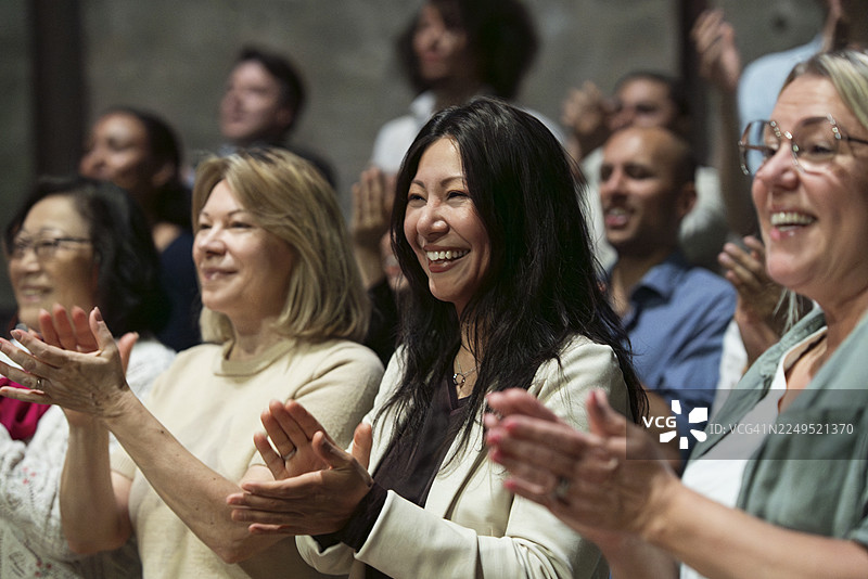 一位成熟的女士在舞台剧院里站着鼓掌，脸上带着笑容图片素材
