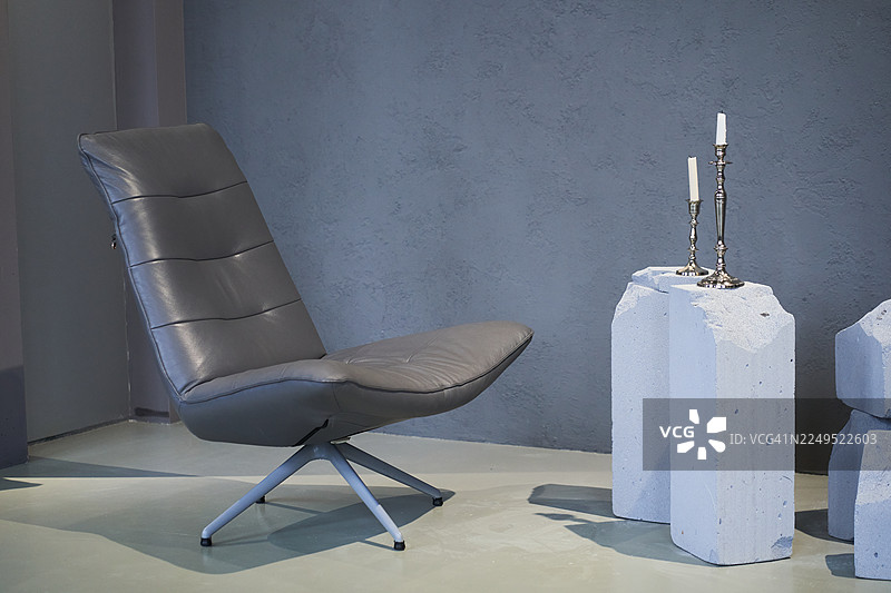 室内的一部分。灰色椅子搭配带蜡烛的混凝土咖啡桌。灰色墙壁背景。图片素材