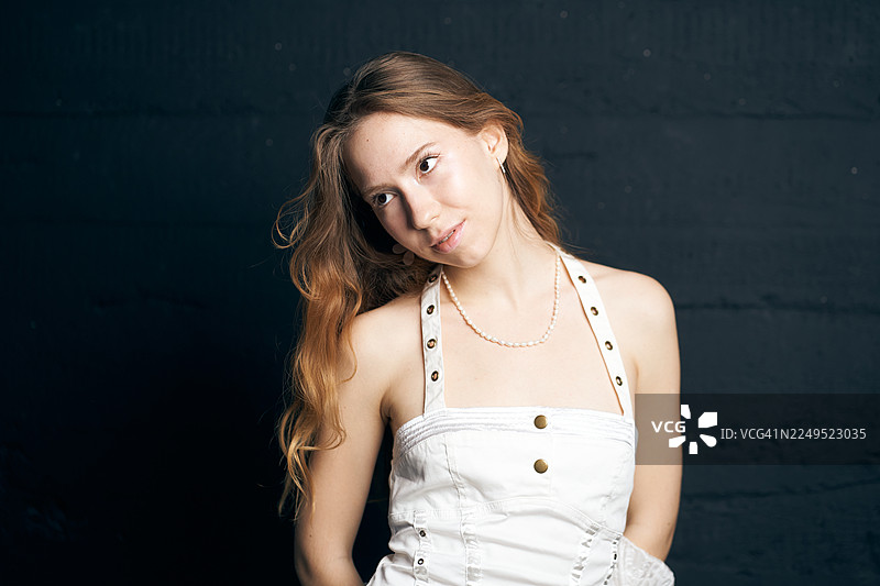 身着白色服装的年轻女子在影棚风格的人像摄影中，摆姿势面对深色纹理墙壁。2026年度代表色图片素材