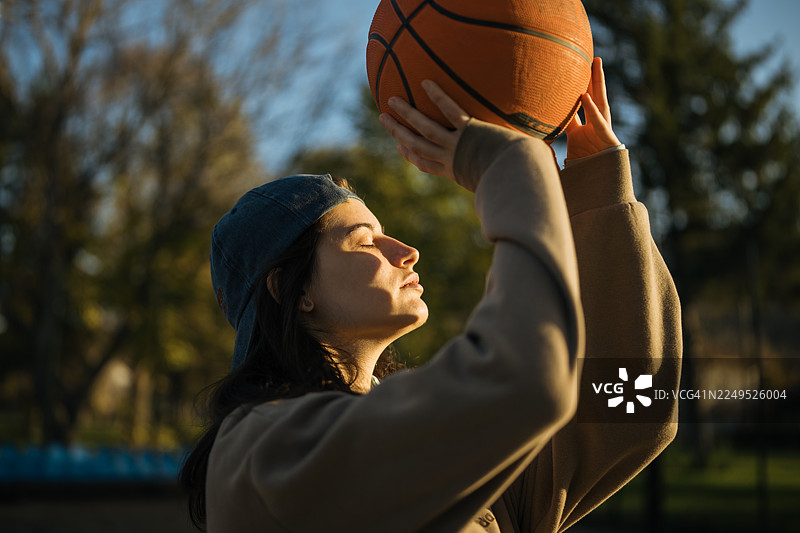 街头篮球场上，一位嘻哈风格的女性的肖像，她手中拿着一个篮球。图片素材