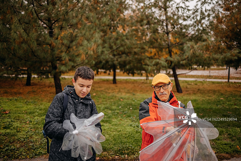 下雨天，一位老人与他的十几岁的孙子在公园见面，并撑开了一把伞。图片素材