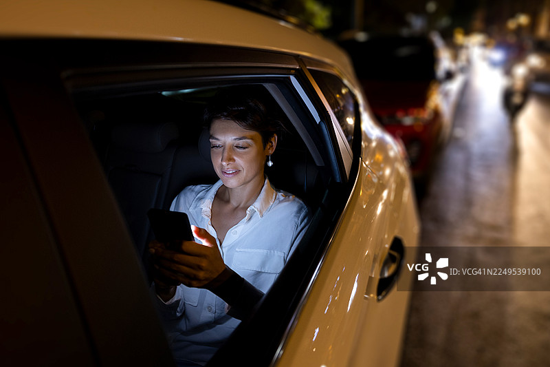 夜间，一位女士在繁忙的城市街道上，在车内使用智能手机。图片素材