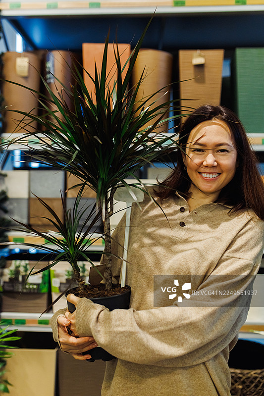 一位女士微笑着拿着一盆龙血树，准备用它来装饰家居和办公空间图片素材