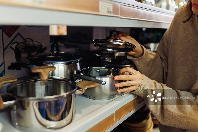 顾客在厨具店的展示架上浏览并拿起锅盖图片素材