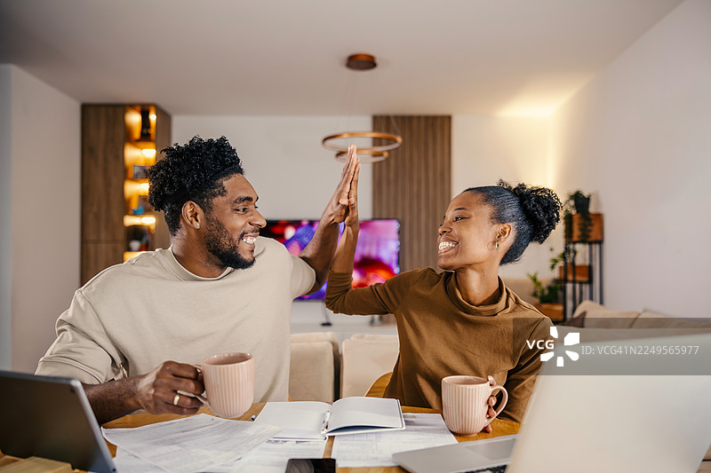一对快乐的夫妇在家中击掌庆祝，讨论财务问题图片素材