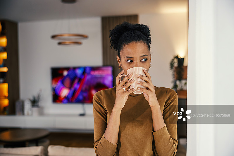 一位女士在客厅里喝咖啡，若有所思图片素材