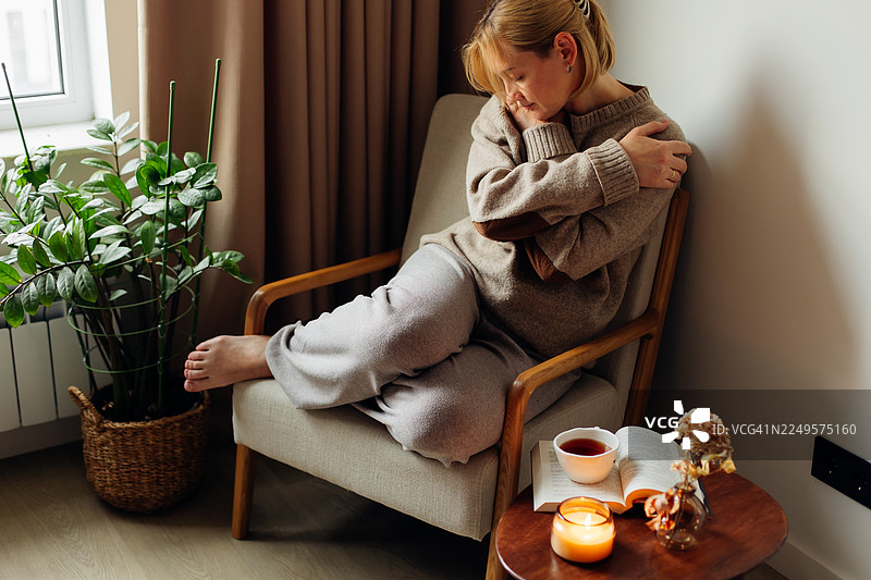 温馨宁静的早晨：女子在家中，手捧茶杯，伴着书籍与蜡烛，悠闲放松图片素材