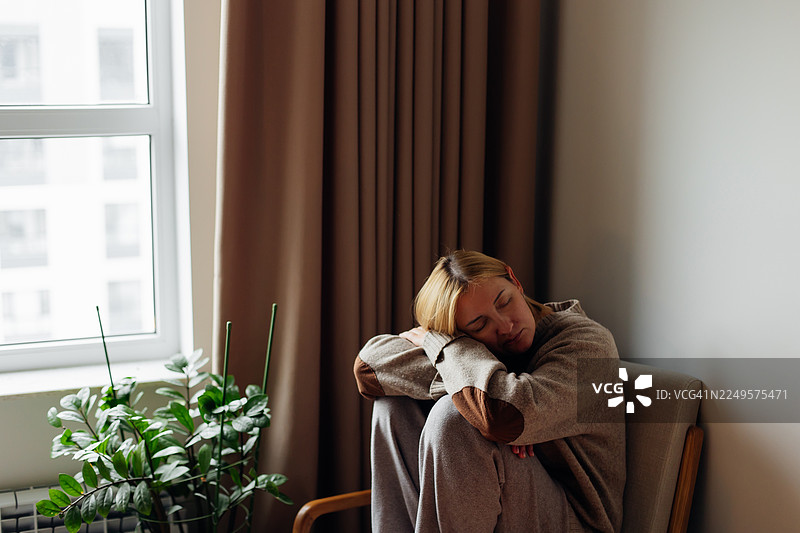 一天劳累后，女子在家中窗边椅子上休息，享受宁静的沉思时刻图片素材