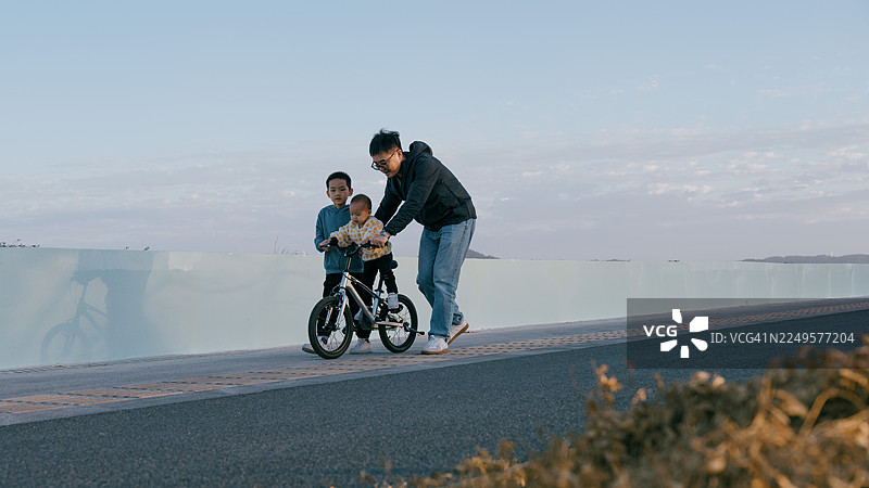 一位亚洲父亲在海边和孩子们玩耍骑自行车；亚洲家庭生活方式图片素材