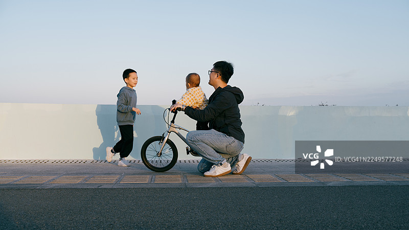 一位亚裔父亲在海边和孩子们玩耍并骑自行车；亚裔家庭生活方式图片素材