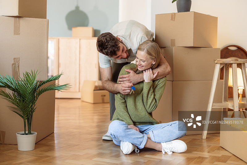 一对年轻夫妇在新家拆箱，拥抱在一起，周围摆满了搬家用的箱子图片素材