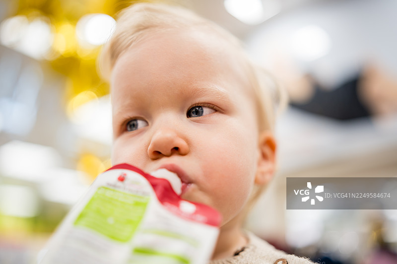 明亮的室内环境中，一个蹒跚学步的孩子正在吃袋装的糊状食物。图片素材