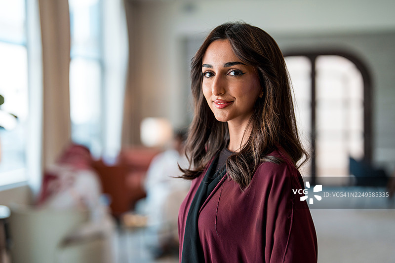 身着勃艮第色阿巴亚的优雅年轻阿拉伯女商人，身处现代酒店大堂图片素材