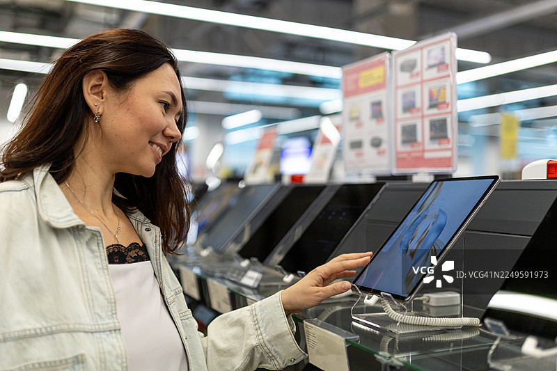 女士在电子产品商店购物，在一个产品信息亭的数字触摸屏上操作图片素材