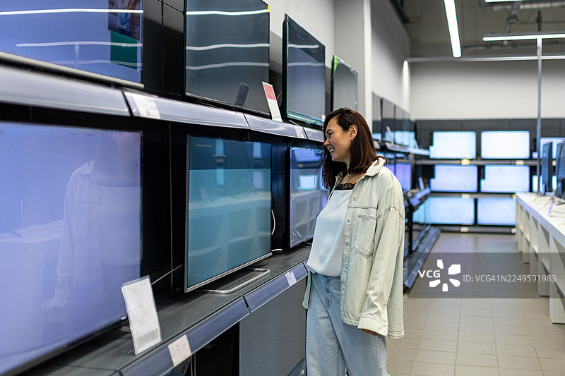 一位女士在电器商店选购电视，正在查看大型平板电视。图片素材