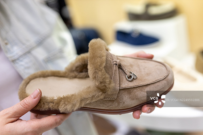 温暖舒适的米色毛绒拖鞋，由双手捧着，适合居家穿着，带来舒适与放松图片素材