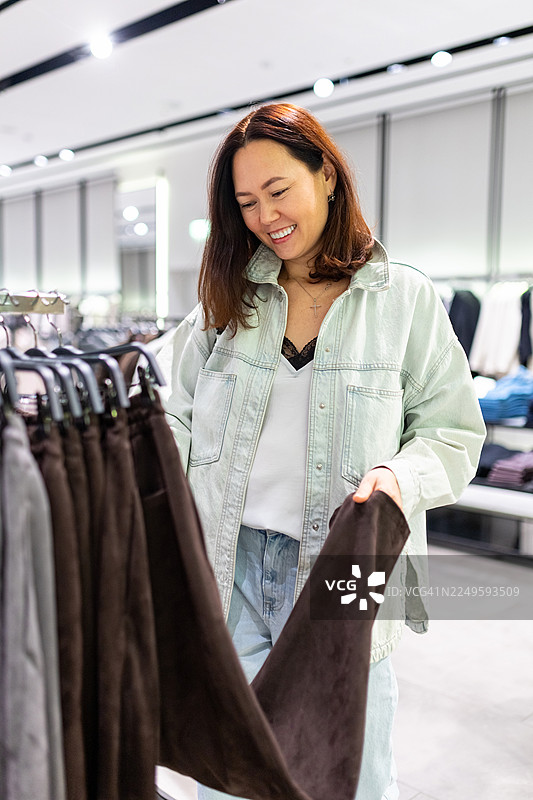 一位穿着浅色牛仔夹克的女士在服装店开心地挑选裤子图片素材