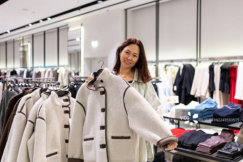 一位女士在现代时尚店里开心地选购一件温暖的抓绒外套图片素材