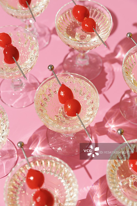 粉色背景上，重复排列的香槟水晶杯和鸡尾酒樱桃图片素材