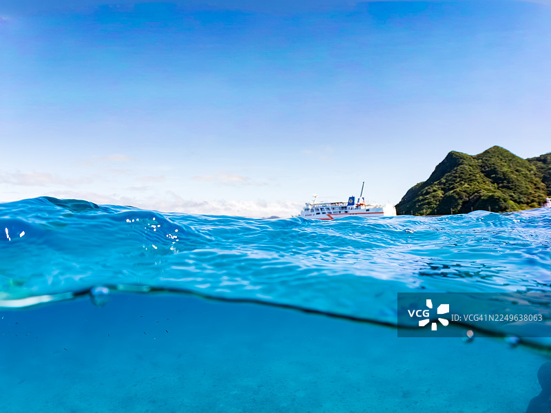 从美丽的珊瑚礁海面拍摄的渡嘉敷岛渡轮“座间味”号和古座间岛的美丽半水景。成群的热带鱼。美丽的珊瑚礁和游泳的人们。阿嘉海滩,阿嘉岛,冲绳,庆良间图片素材