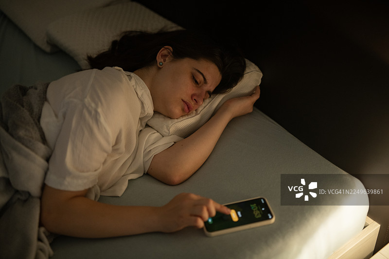 疲倦的女人正在关掉闹钟。图片素材