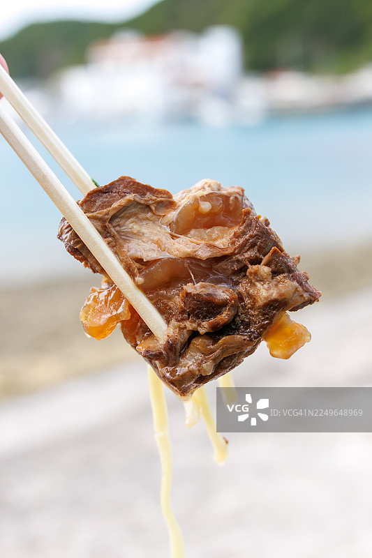 早餐享用一大碗冲绳荞麦面。上面铺满了炖至软嫩的排骨(Sōki),用甜咸酱汁炖煮。搭配三品茶(冲绳风茉莉花茶)。地点位于冲绳座间味港,一个如热带天堂般的偏远岛屿。图片素材