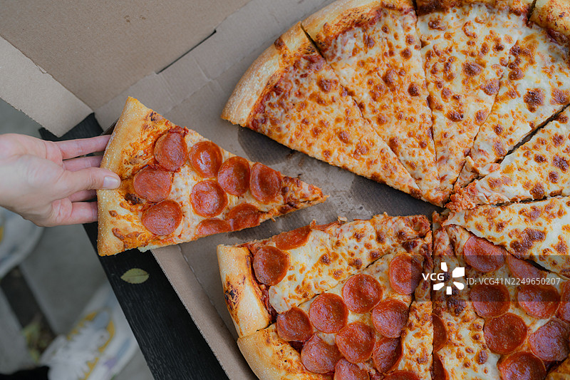 手从盒子里拿一片意大利辣香肠披萨图片素材