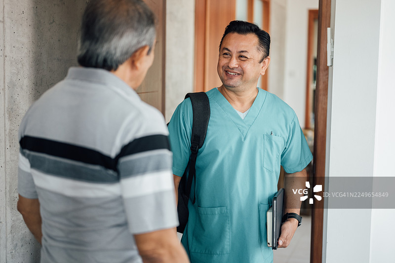 一位年长的亚洲男性打开门，迎接前来家访的亚洲男性心理医生图片素材