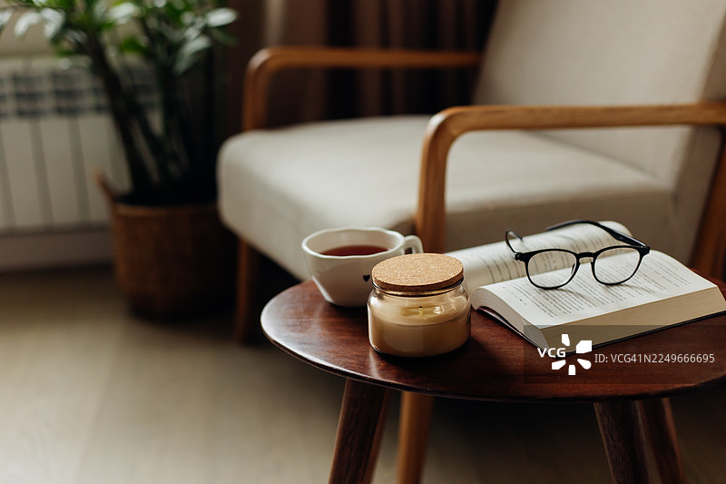 舒适的阅读角落，木桌上放着打开的书、眼镜、茶和蜡烛图片素材