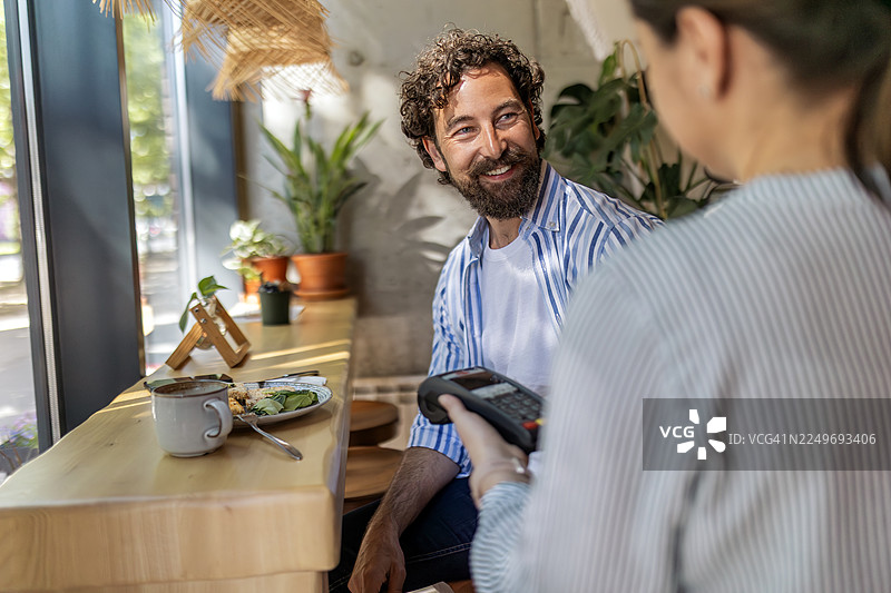 年轻男子在早餐桌旁使用信用卡进行数字支付图片素材