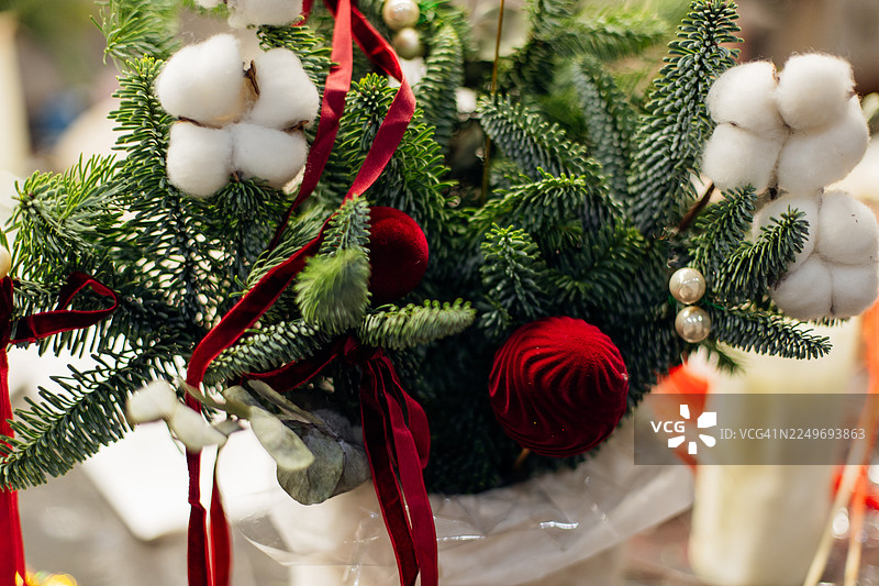 节日圣诞插花的特写，包含常绿枝、白色棉花枝、红色丝绒缎带和装饰品。温馨的节日氛围与舒适的季节性装饰。图片素材