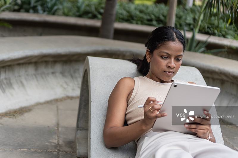 女子在户外长凳上使用带触控笔的数码平板电脑图片素材