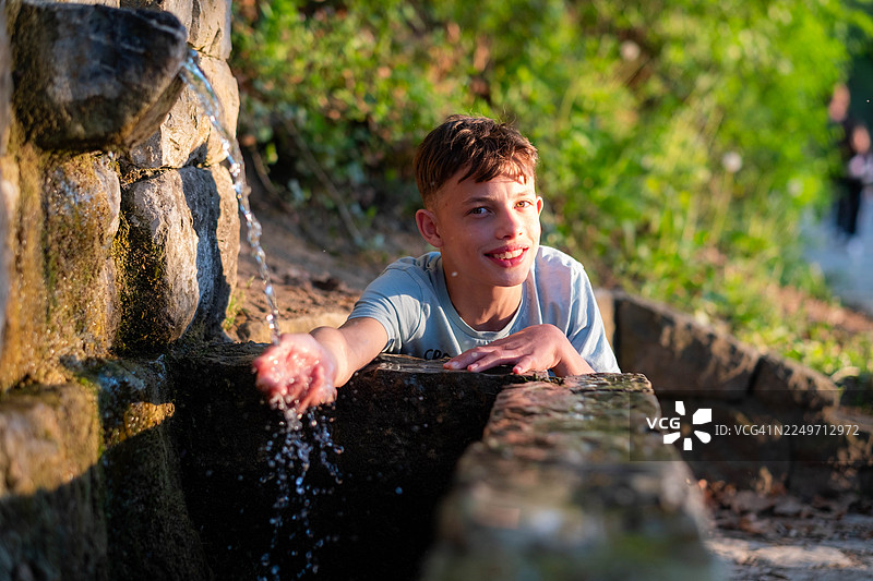 快乐的小男孩在石头喷泉旁玩水图片素材